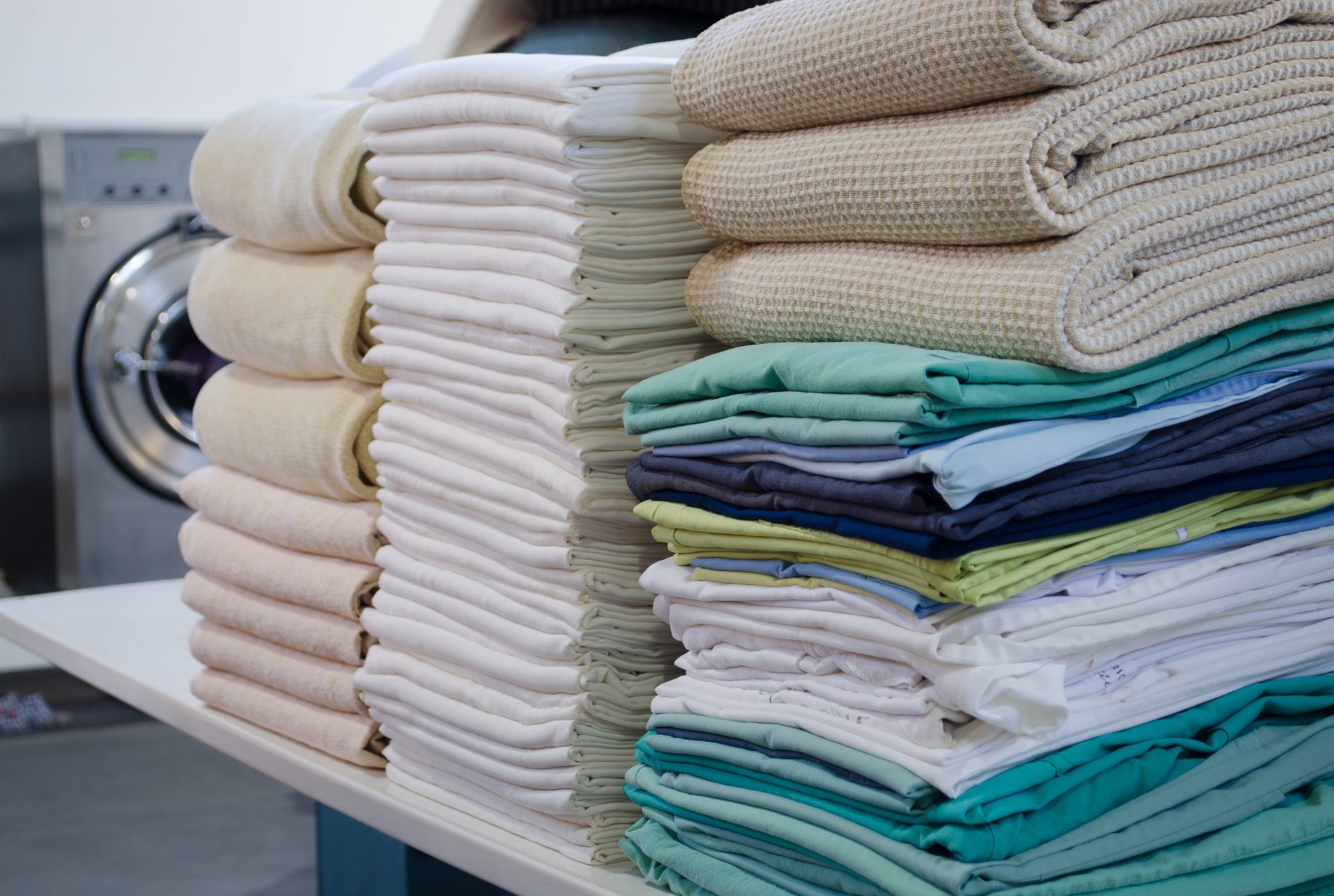 Neatly folded stacks of towels, sheets, and linens on a table in a laundry facility.