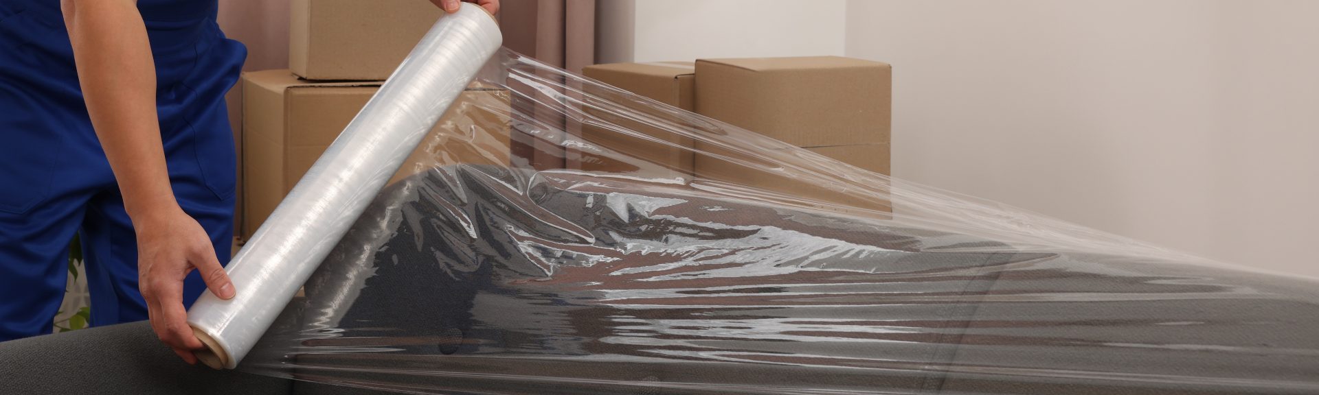 Mover wrapping a couch in clear protective plastic film during packing.