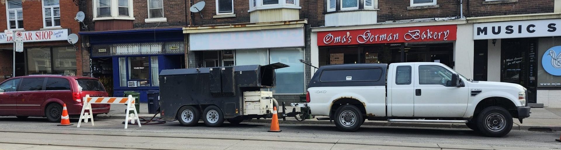 Pickup truck towing heat-treatment equipment trailer parked at curb with safety cones and barricade.